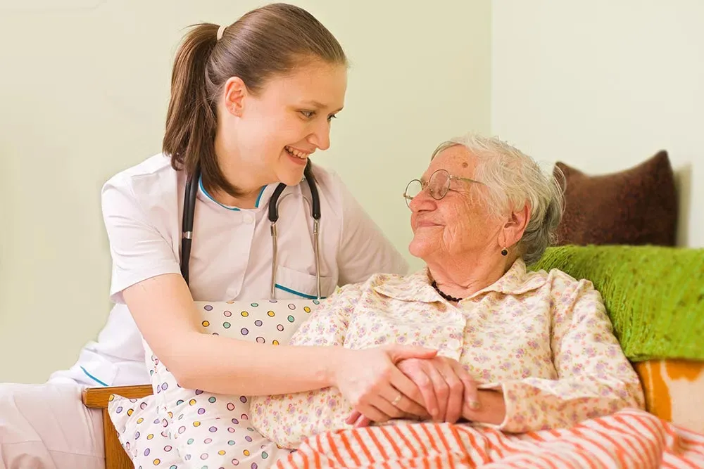 A caregiver gently holding an older patient's hand during an in-home visit